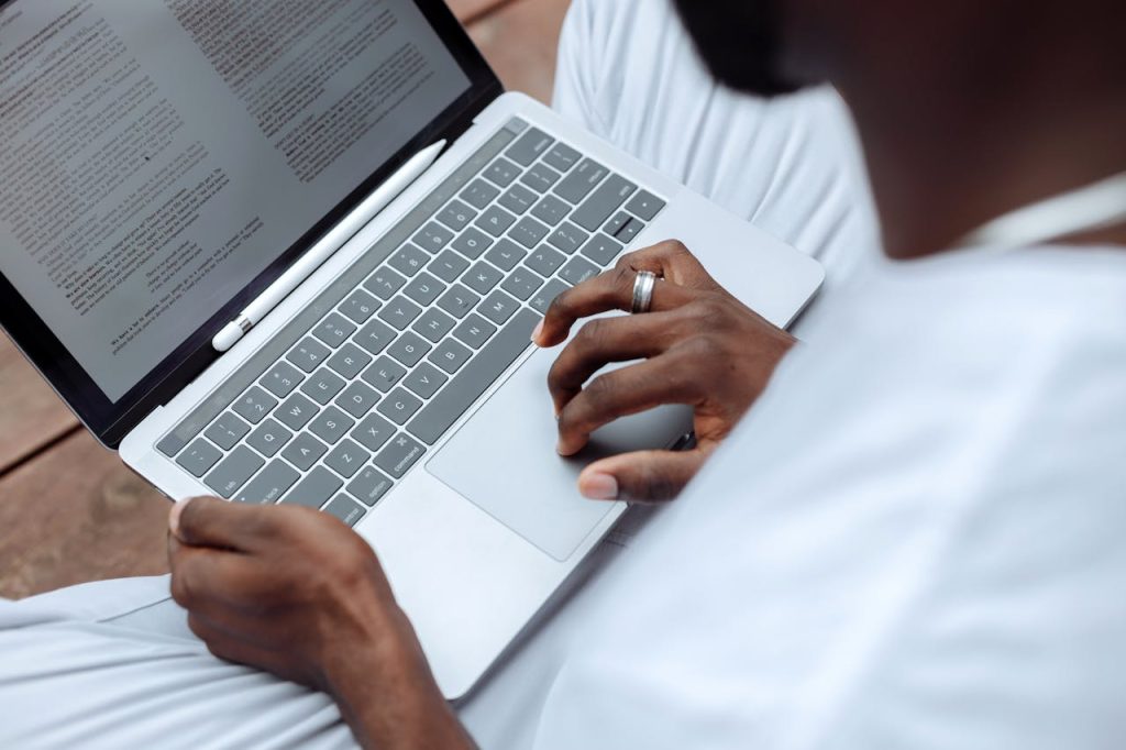 Close-up of a man using a laptop with a stylus pen for reading and working outdoors.